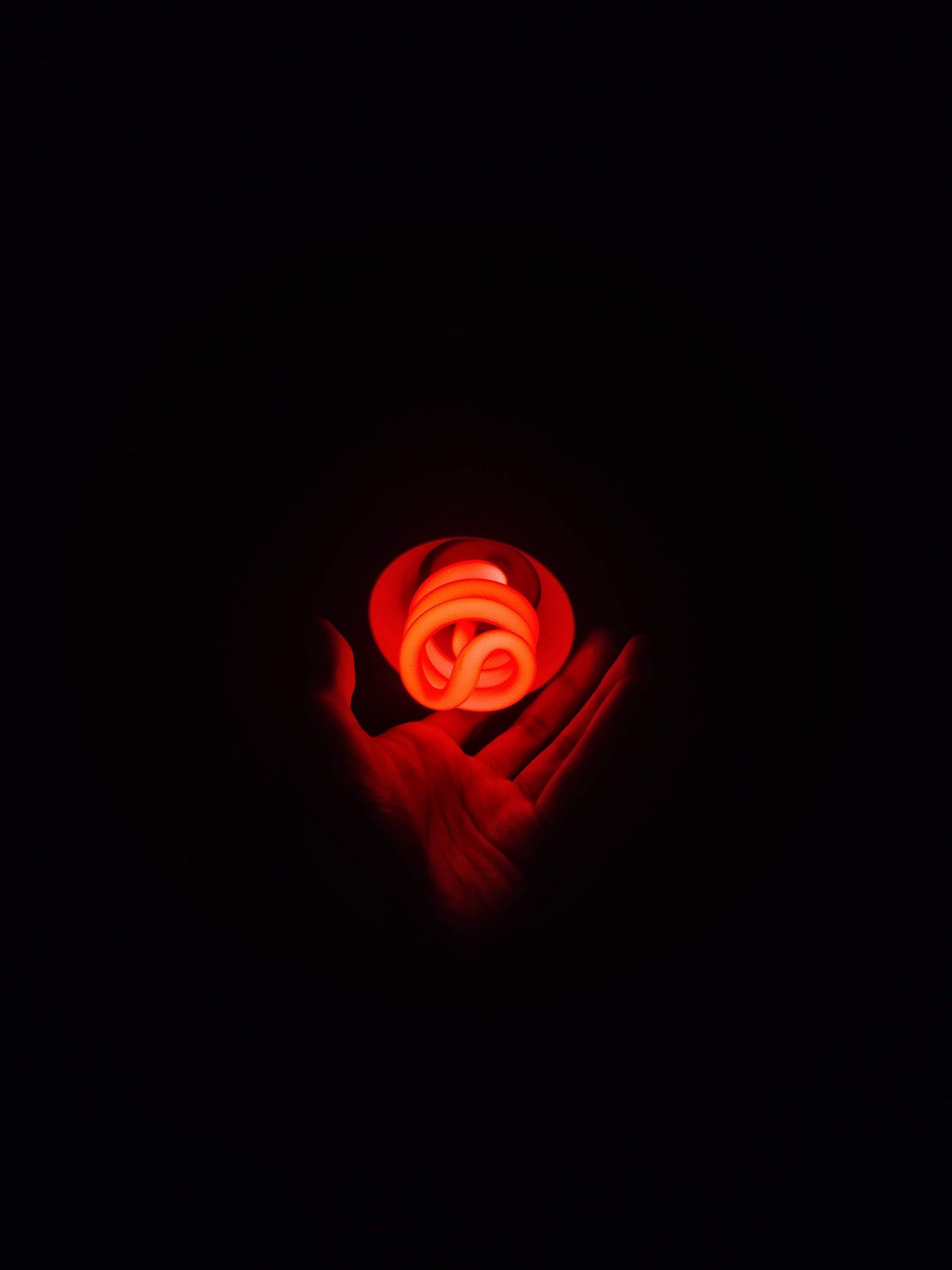 A red glowing compact fluorescent light bulb in a human hand against a dark background.